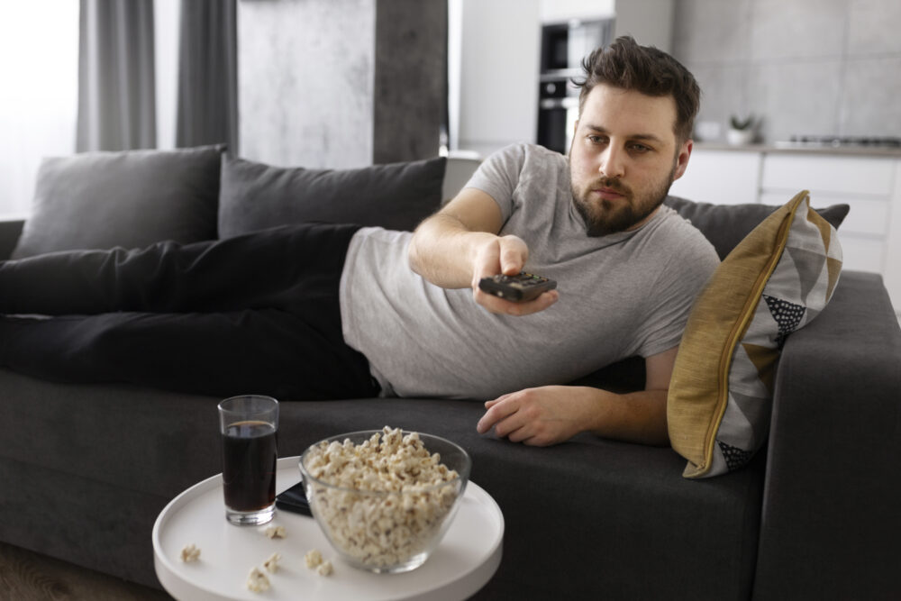 Représentation d'un homme qui regarde la télévision sur son canapé symbolisant l'addiction aux plateformes vidéos.